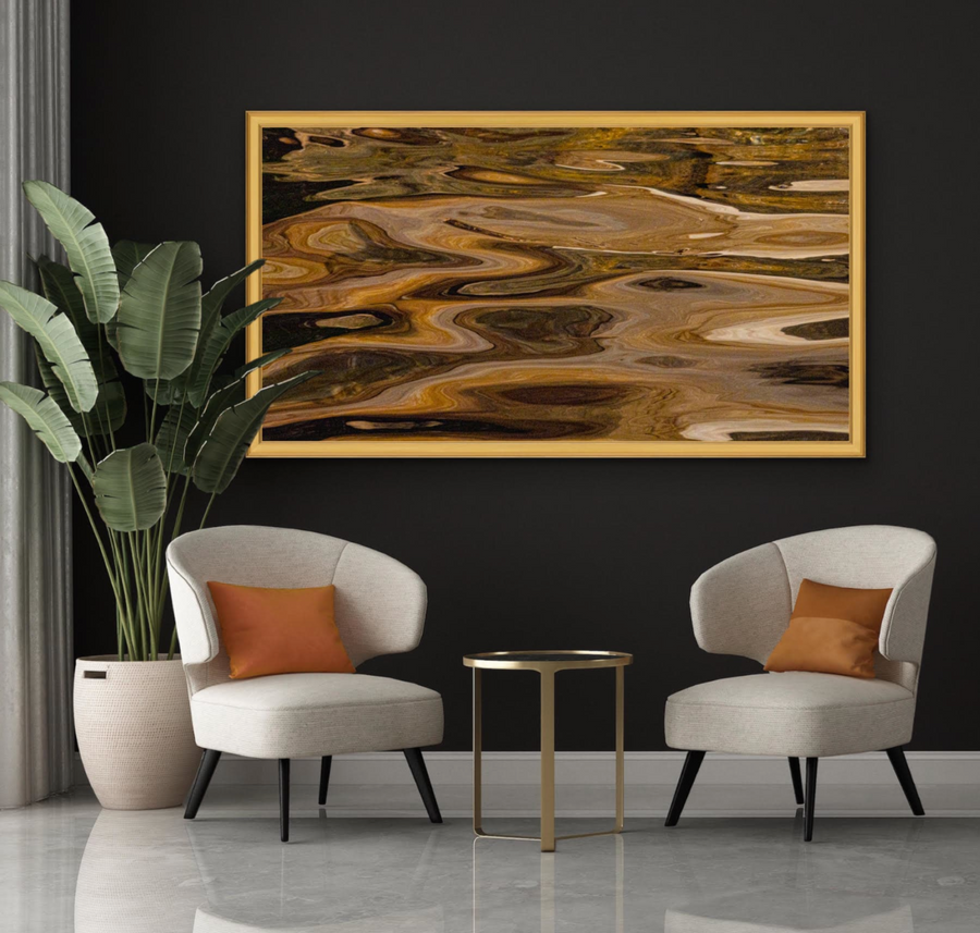 Large framed abstract wall art with swirling gold, brown, black, and cream patterns, displayed above two light beige armchairs with orange pillows in a modern living room setting.