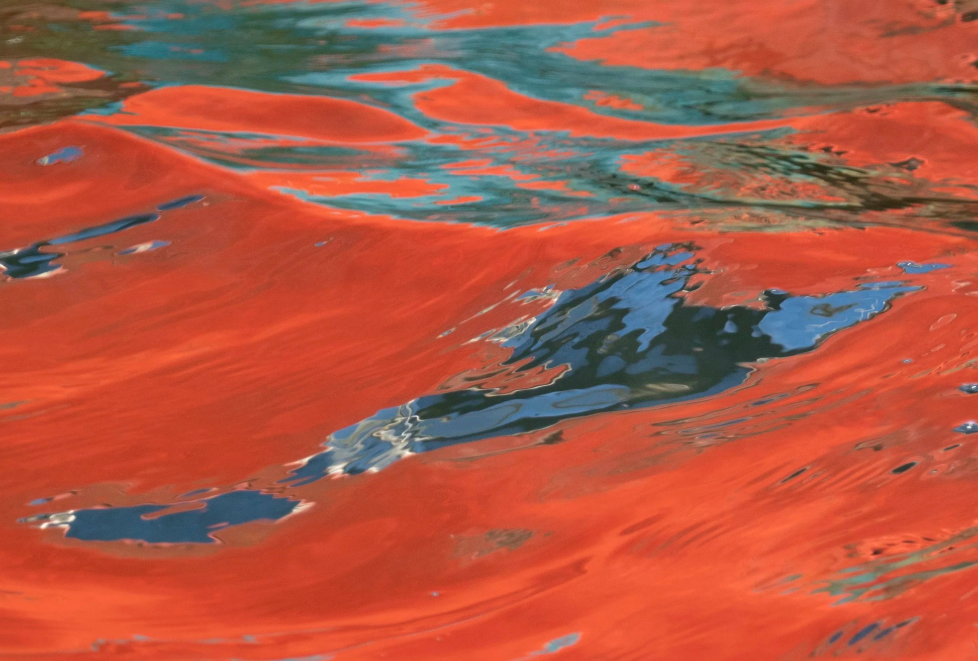 Satellite view of a desert landscape with red sand dunes and blue water.