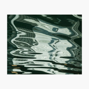 An abstract art print depicting distorted, reflective ripples of light and dark water, framed by a wide white border.