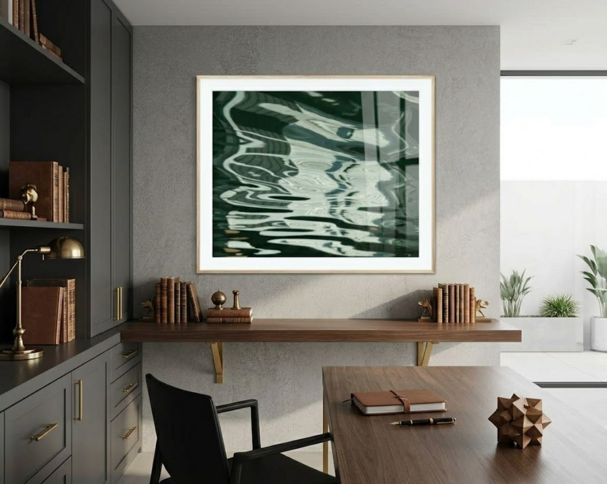 A framed abstract art print featuring green, black, and white fluid wave patterns, displayed on a gray wall in a modern, stylish home office setting with a desk, chair, and bookshelves.