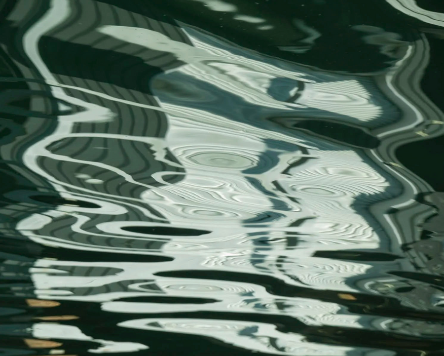 Abstract close-up of rippling water with distorted reflections in dark green, black, and pale gray tones.